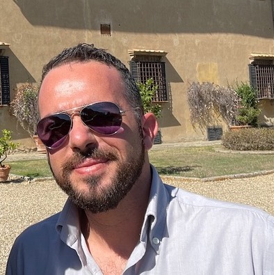 Davide Rago con occhiali da sole in esterno, davanti a una villa toscana, simbolo del suo legame con il territorio agricolo